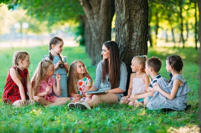 children-and-education-young-woman-at-work-as-educator-reading-book-to-boys-and-girls-in-park_109285-495